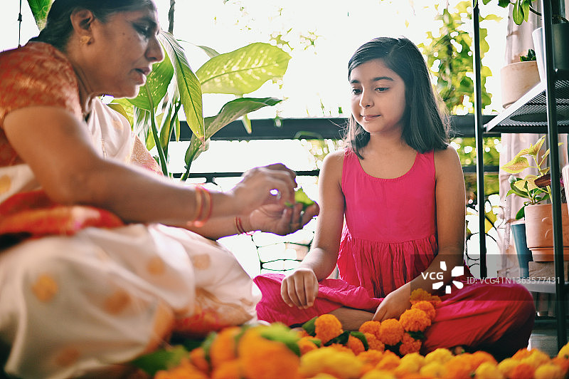 祖母教孙女在客厅制作万寿菊花环图片素材