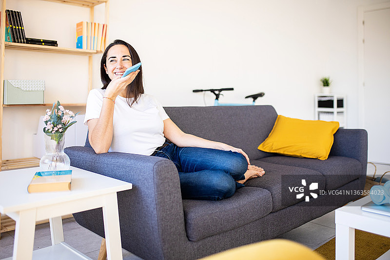 年轻女人在家中沙发上放松，用智能手机发送语音消息图片素材