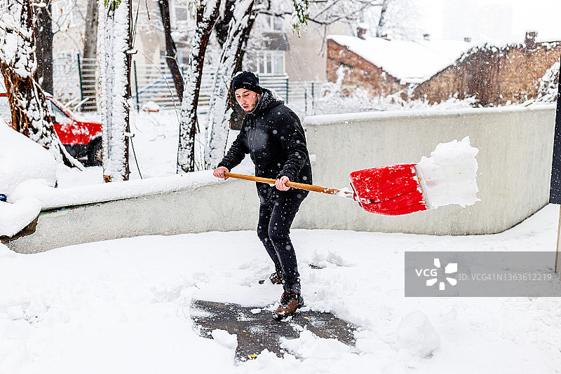 在房子前用铲子清理积雪的年轻男人图片素材