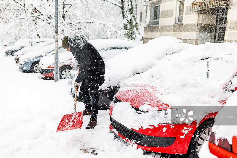 年轻男人用铲子在车前铲雪图片素材