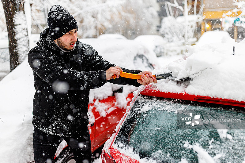 一个年轻男子用铲子清理汽车上的积雪图片素材