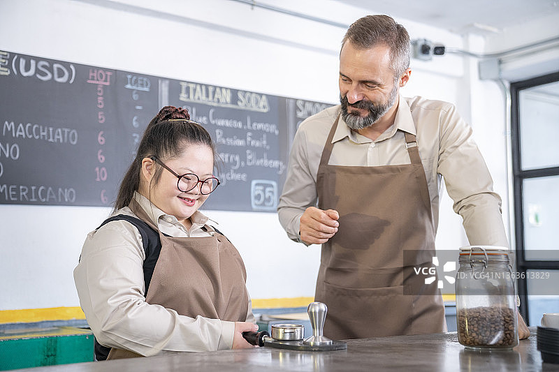 白人男咖啡师和唐氏综合症实习生在café吧台煮咖啡。图片素材
