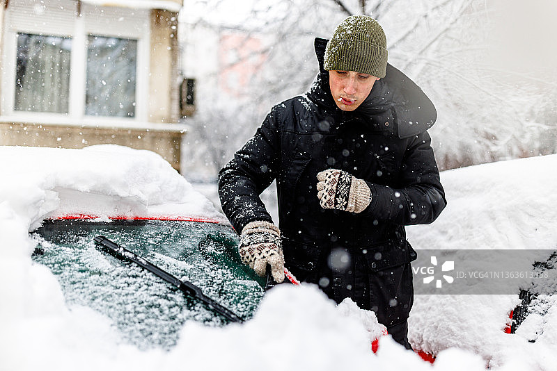 年轻男子正在清理汽车挡风玻璃上的冰雪图片素材
