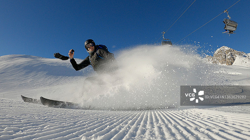 男子在阳光明媚的阿尔卑斯山上滑雪，雪花飞溅图片素材
