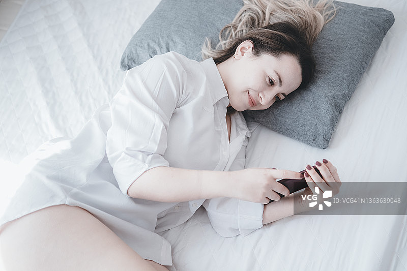 面带微笑的女人在床上使用智能手机图片素材