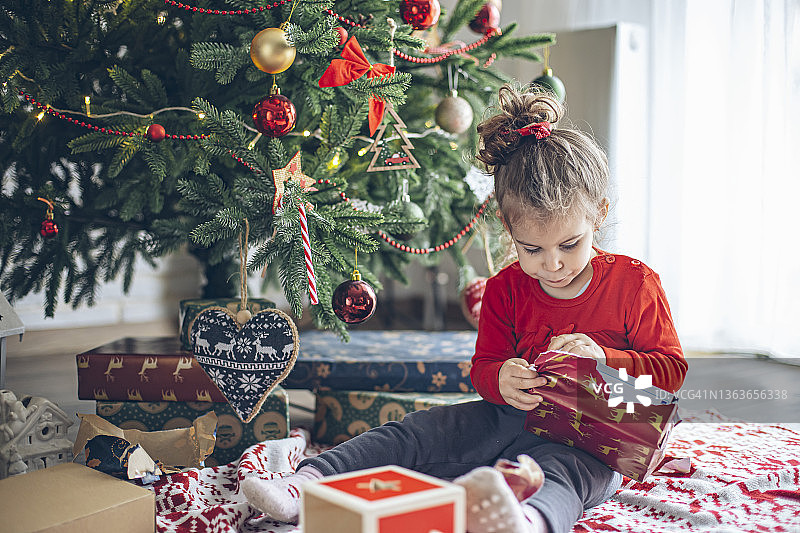可爱的小女孩在圣诞节的早晨打开礼物图片素材