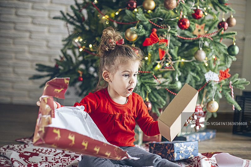 可爱的小女孩在圣诞节的早晨打开礼物图片素材