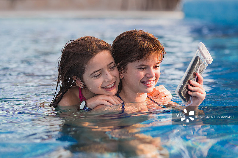 快乐的女孩们在游泳池自拍时拥抱图片素材