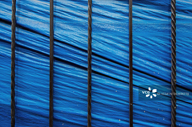 蓝色塑料粗麻布防水布屏衬托的黑色扭曲金属杆栅栏图片素材