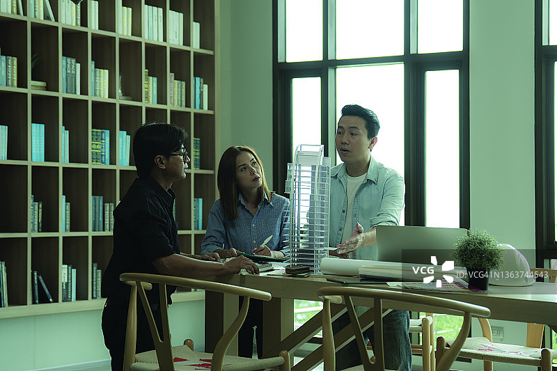 建筑师在办公室讨论建筑项目，共同研究新建筑模型图片素材