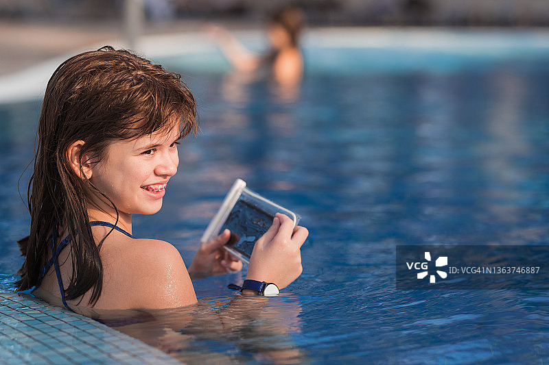 在游泳池拿着手机微笑的牙套女孩图片素材