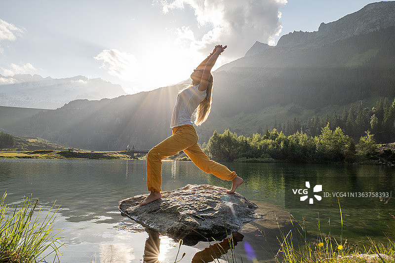 年轻女子在湖上方的岩石上练习瑜伽图片素材