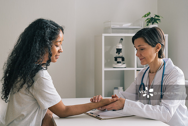 中年女医生检查非裔美国患者的脉搏，医疗保健检查预约图片素材