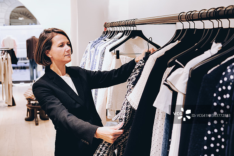 年轻女子在服装店挑选衣服，在意大利精品店购物图片素材