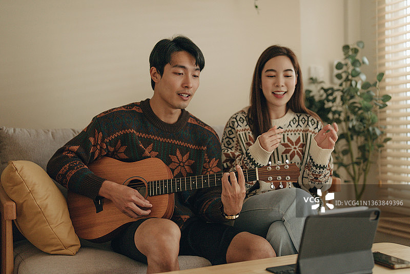 年轻男人在家弹吉他，年轻女人唱歌互动图片素材