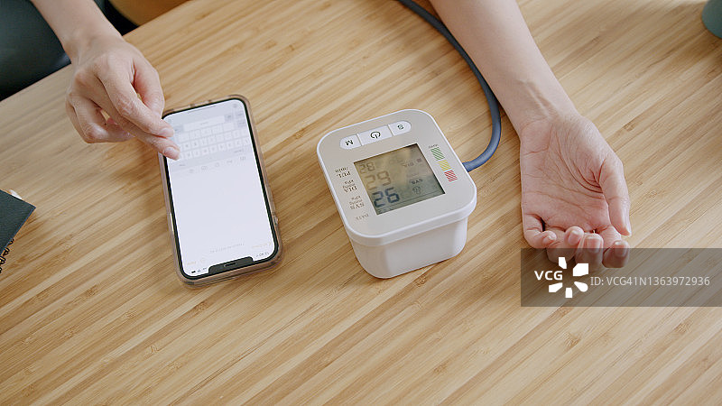 亚洲女人在家用智能手机记录血压监测仪上的血压和心率数据图片素材
