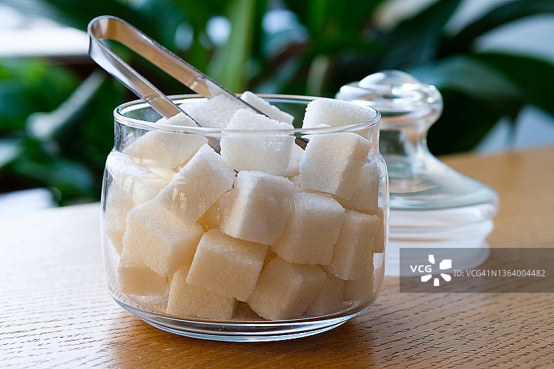 透明玻璃糖罐中的方糖，在家里、咖啡馆、自助餐厅或餐馆的木桌或背景上，不良营养和生活方式的概念图片素材
