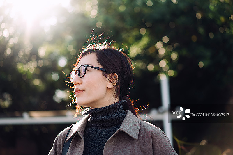 年轻漂亮的亚洲女性在公园里散步，在户外享受阳光的温暖，呼吸新鲜空气，在树下放松身心图片素材