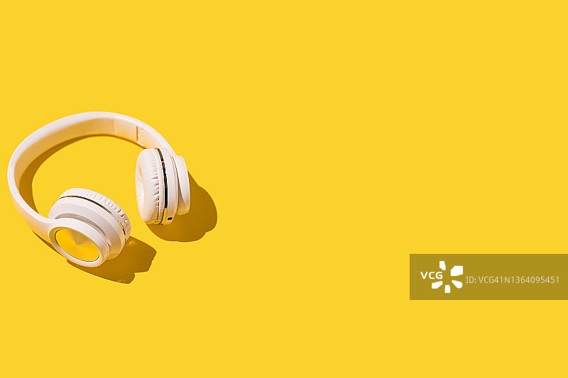 黄色背景左侧的白色无线耳机与硬阴影：音乐、耳机、广播、播客概念图片素材