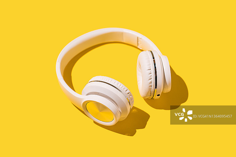 黄色背景上带有硬阴影的白色无线耳机。音乐、耳机、广播、播客、收听和放松活动的概念。图片素材