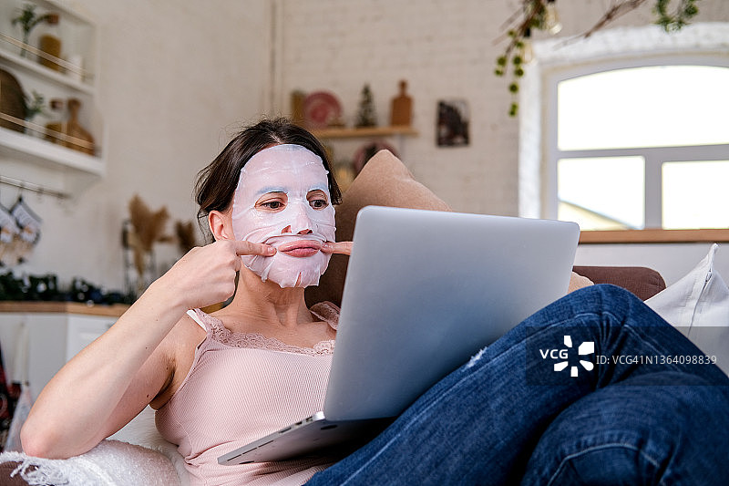 在家远程工作或教育，一位年轻女子正在做保湿面膜并看着笔记本电脑屏幕。居家水疗图片素材