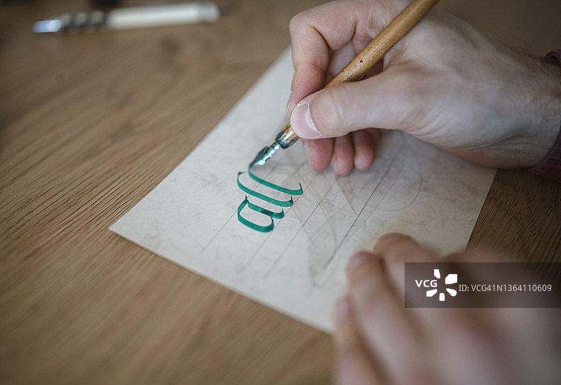 年轻男人用绿色墨水在纸上练习书法图片素材