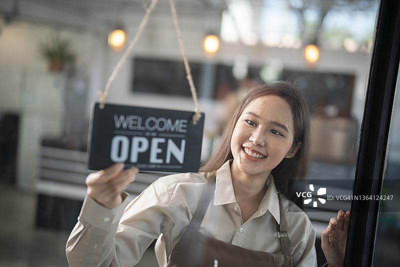 初创咖啡店或餐厅的女老板转动门上的“营业中”标志图片素材