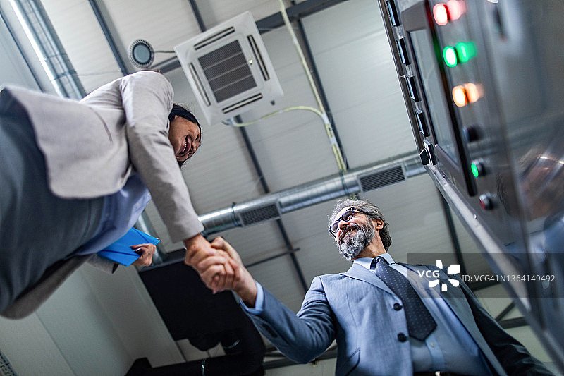 工厂里达成协议的快乐的商务人士仰视视角图片素材