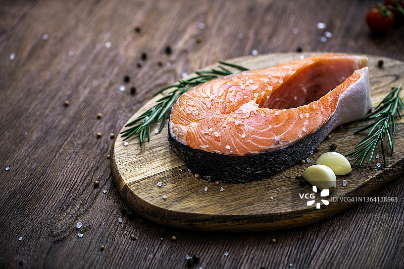 三文鱼：配有番茄、迷迭香和大蒜的生鳟鱼排，置于木桌上图片素材