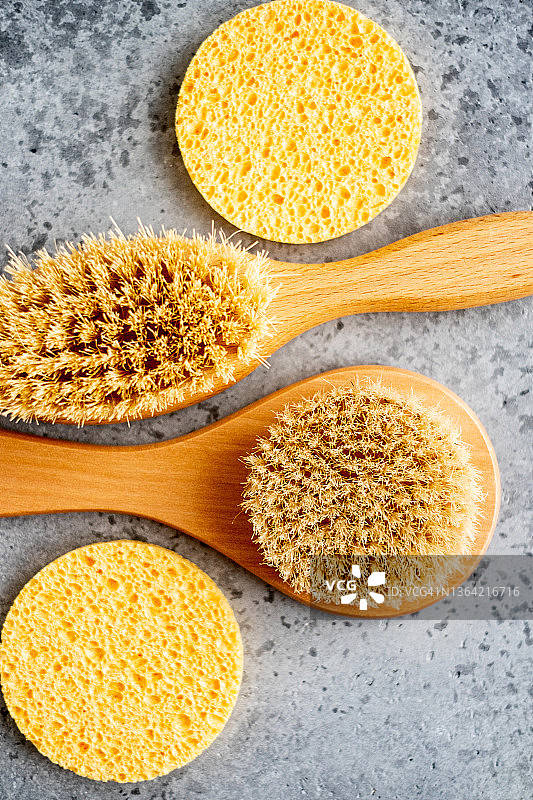 灰色水泥背景上的干性皮肤刷和圆形清洁海绵特写，俯视图片素材