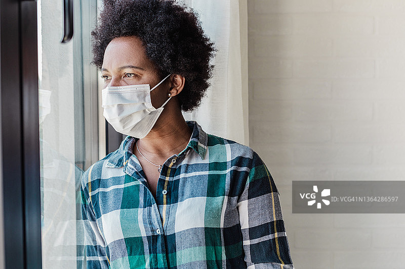在家里窗边戴着防护面罩的非裔美国女人图片素材