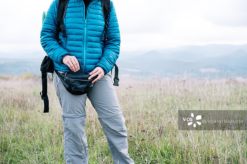 在乡村景色中将笔记本放入腰包的女性背包客图片素材