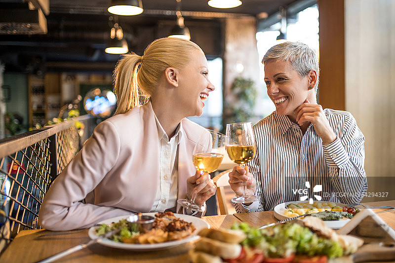 快乐的年轻商业伙伴在餐厅一起享用午餐并用葡萄酒敬酒图片素材