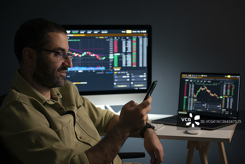 男子在智能手机和桌面上查看股市数据图片素材