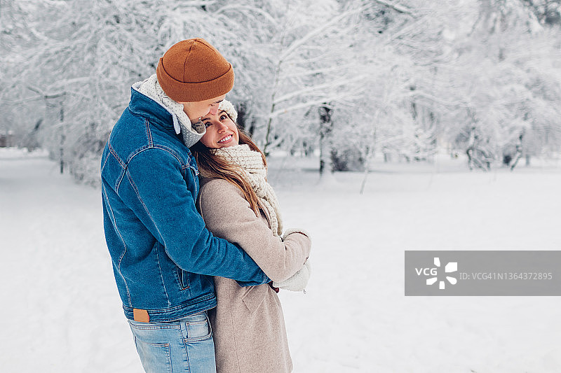 情人节：年轻情侣在冬季公园漫步，拥抱欣赏雪景图片素材