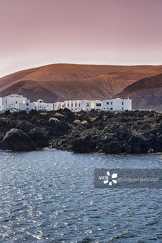 西班牙兰萨罗特岛奥尔佐拉，岩石熔岩海岸上的白色房屋，黑色火山岩，傍晚的天空图片素材