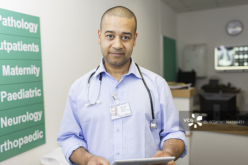 自信的男医生在医院走廊里使用平板电脑图片素材