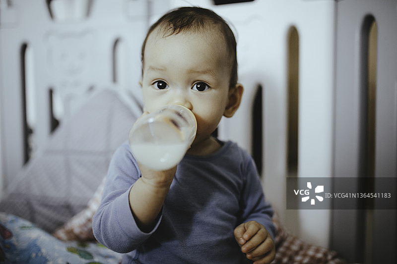 可爱的亚洲宝宝坐在床上喝奶图片素材