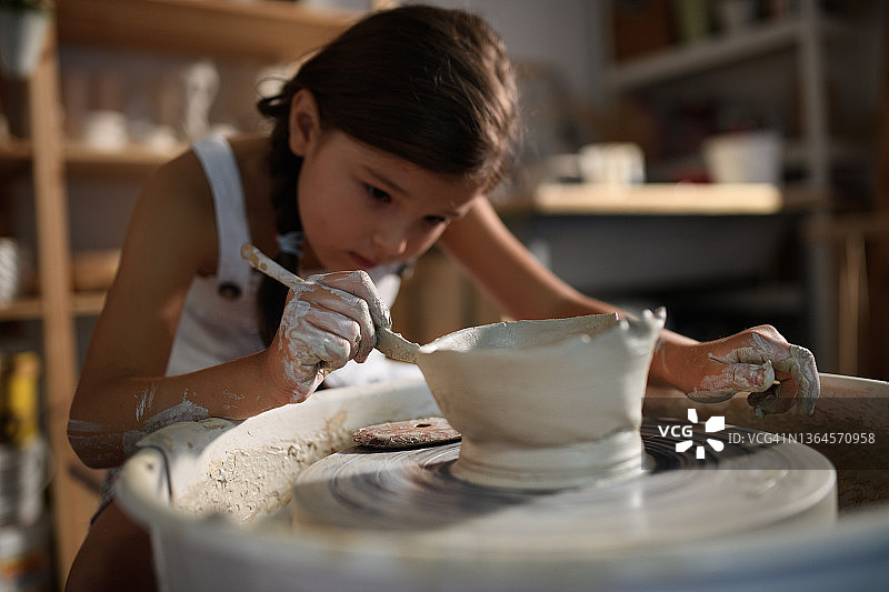 专心的小女孩在艺术工作室的陶轮上制作陶器图片素材