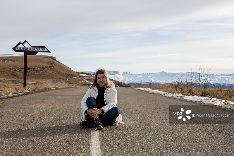 一位女游客正坐在路上，欣赏着山川的自然风光。自由的概念，旅行，生活方式。图片素材
