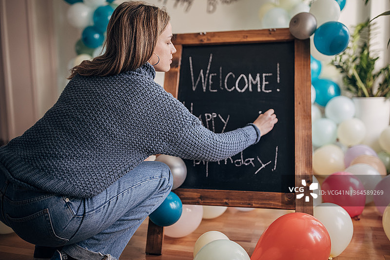 年轻女子在黑板上书写生日派对欢迎标语图片素材