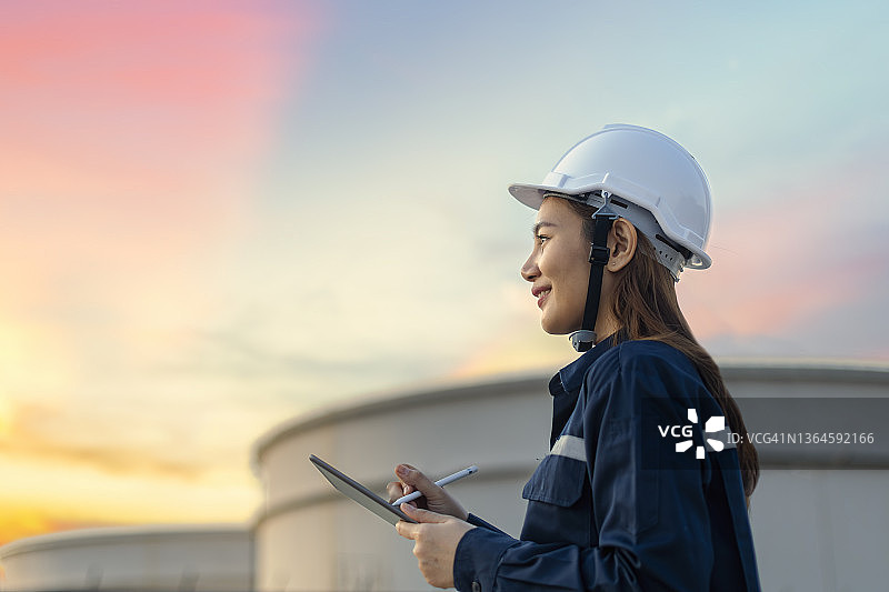 石油炼油工程师在石油和天然气工业中使用个人安全防护设备PPE，通过平板电脑检查清单。经典能源商业概念。图片素材