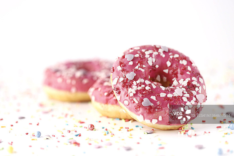 白色背景下，一堆带有粉红色糖霜和彩色糖屑的甜甜圈特写图片素材