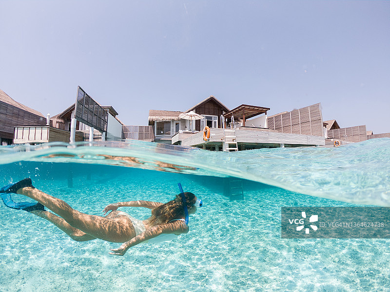 女人在热带海洋中潜水，水下分屏拍摄，背景是水上别墅图片素材