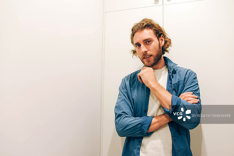 一位英俊的络腮胡男子站在明亮的房间里，身穿牛仔衬衫，外形俊美，留着长发，休闲风格。图片素材