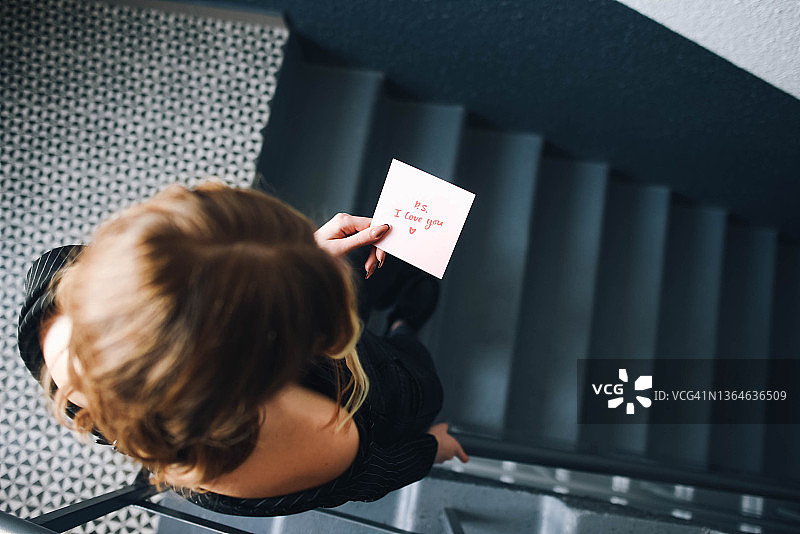 女孩站在楼梯上读便条。情人节，灰色背景，女人的手，爱的表白，情书，告白信，带便条的女孩，女孩在阅读图片素材