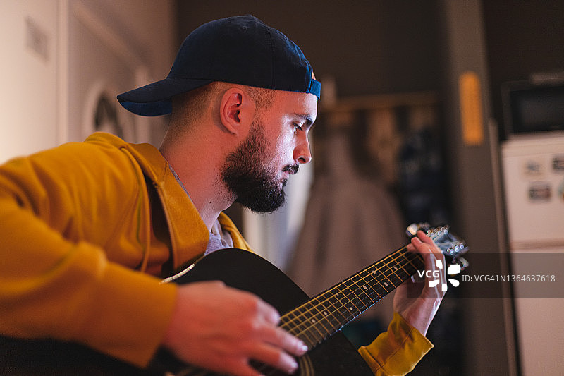 特写：年轻的络腮胡男子在家中弹奏吉他，学习新歌图片素材