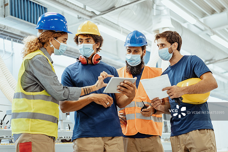 疫情期间工厂员工佩戴口罩，使用平板电脑进行简短会议图片素材