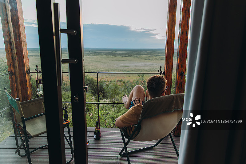 在纳米比亚埃托沙国家公园的旅馆露台上，男子旅行者凝视着狂野稀树草原的日落图片素材