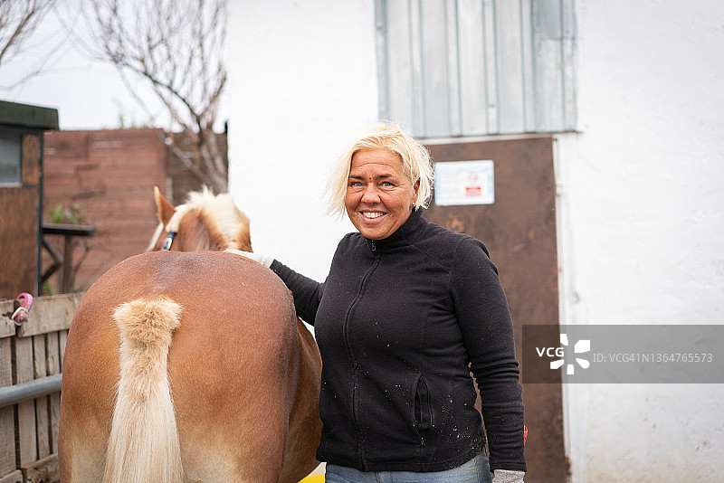 中年妇女站在马厩里，靠近马匹，对着镜头摆姿势图片素材